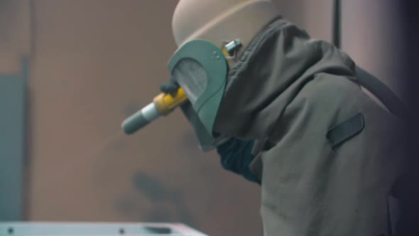 worker wearing mask using sand blast on metal surface in workshop