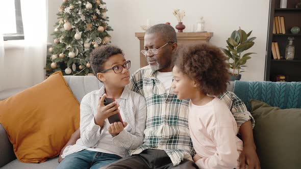 Carefree African American Boy and Girl Resting on Sofa with Grandfather and Web Surfing in Internet