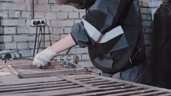 Young Man Worker in Protective Helmet Welding Parts of the Metal Detail Together at the Table