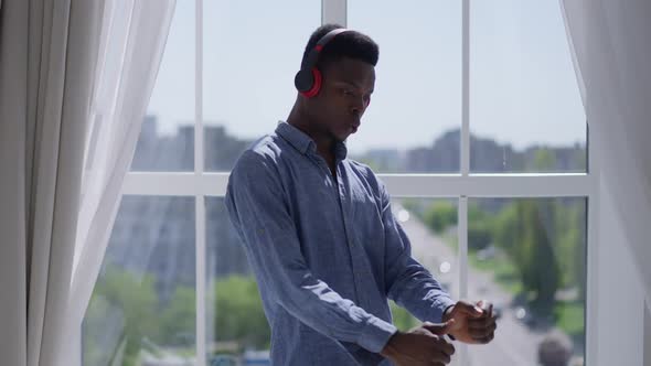 Middle Shot of Joyful Young Man in Headphones Dancing and Singing at Window in Home Office