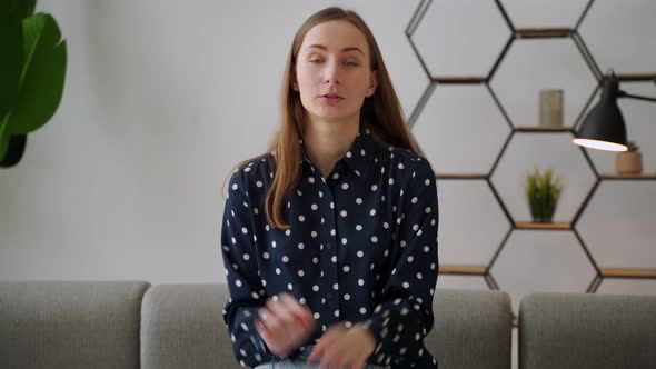 Young Happy Caucasian Woman Speaks While Looking at the Camera While Sitting on the Sofa in the