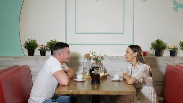 Young People Talk and Drink Tea at Wooden Table in Cafe