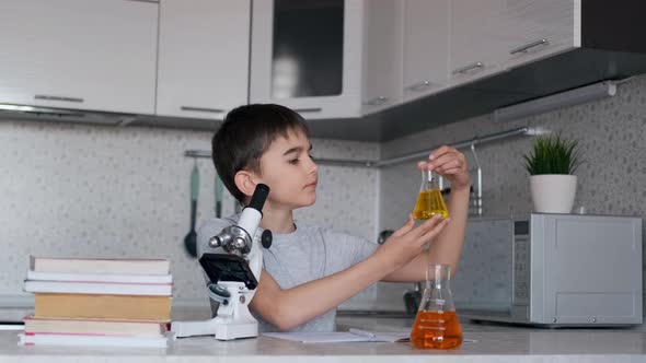 The Boy Learns Biology Using a Microscope and Flasks with Liquid and Makes Notes in a Notebook alt