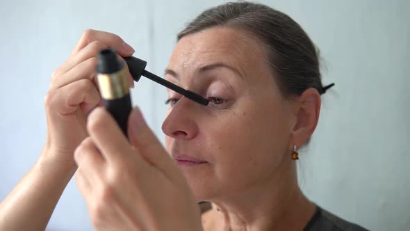 Senior brunette woman paints eyelashes with mascara