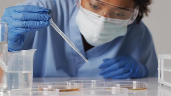 Video of biracial female doctor with face mask using pipette on blue background