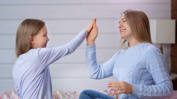 Smiling European Young Woman and Cute Child Girl Playing Clapping Hands Sitting on Bed in Bedroom