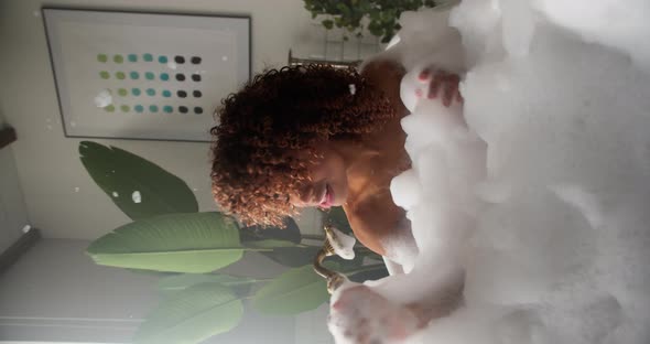 A Funny Woman Sits in a Tub Filled with Foam Holding a Shower and Singing Songs