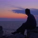 Young Man Waits for the Sunrise at the Sea. Blue hour twilight, gazing at the horizon. Middle Shot - VideoHive Item for Sale