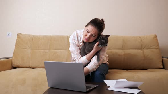 Unhappy Lady Calculates Payments on Laptop Hugging Grey Cat