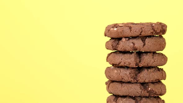 Stack of Oatmeal Cookies with Cocoa Chocolate and Hazelnuts Rotating on Yellow Background