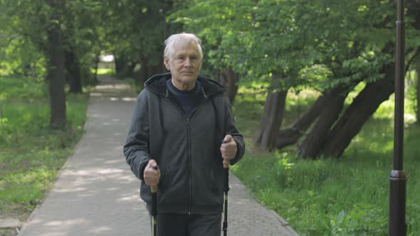 Active Senior Old Man Training Nordic Walking with Ski Trekking Poles in Park