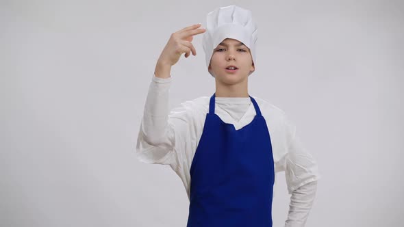 Confident Little Caucasian Chef Showing Tasty Gesture Looking at Camera Smiling