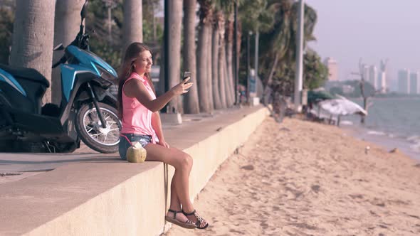 Young Girl with Long Hair Sits on Parapet Makes Selfie