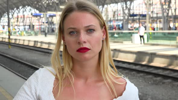 A Young Beautiful Woman Looks at the Camera on a Train Station Platform - Closeup