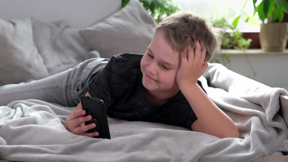 Positive Boy Smiling and Talking By Video Call Sitting on Bed in His Room