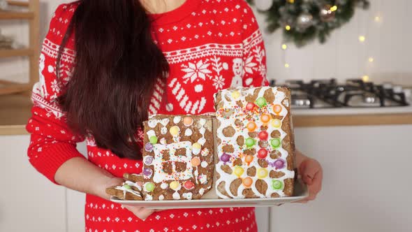 Woman Holds Gingerbread House Against Christmas Decorations