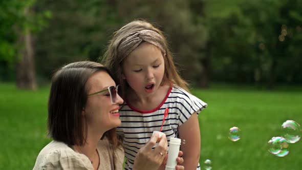 Young Woman and Her 6 Year Old Daughter are Blowing Rainbow Soap Bubbles