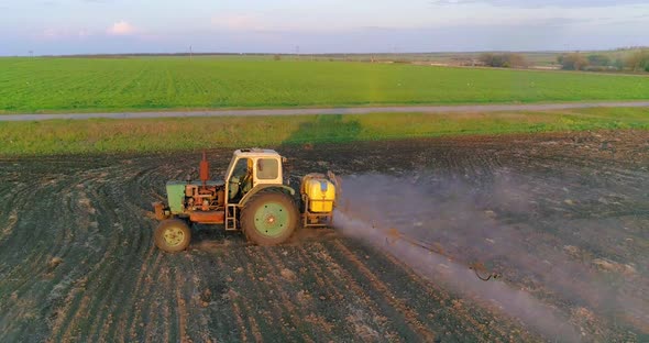 Tractor with trailed sprayer spraying chemicals on agricultural field. Aerial view.