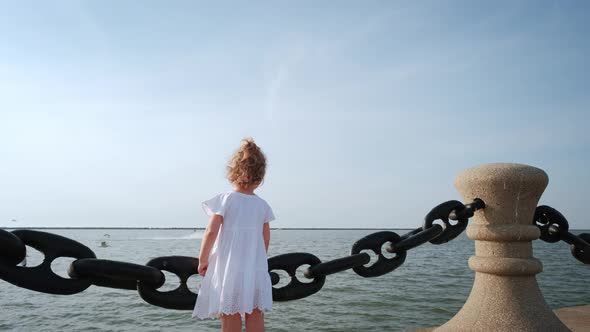 A Little Girl Stands on the Pier and Looks at the Se