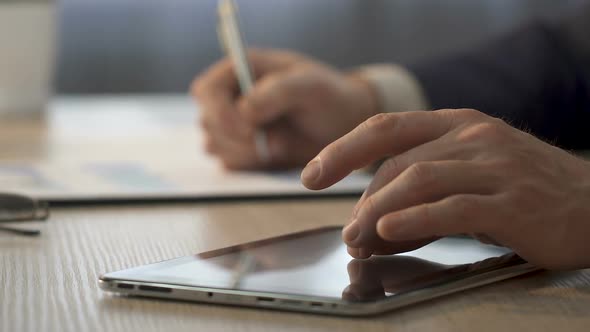 Hands of Businessman Zooming on Tablet, Office Worker Making Notes on Graph