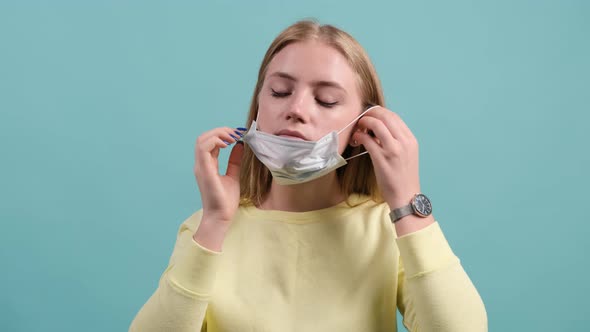 Young Woman Put on Medical Mask on a Turquoise Background.