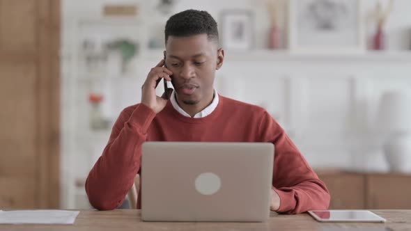 African Man Talking on Phone while using Laptop in Office