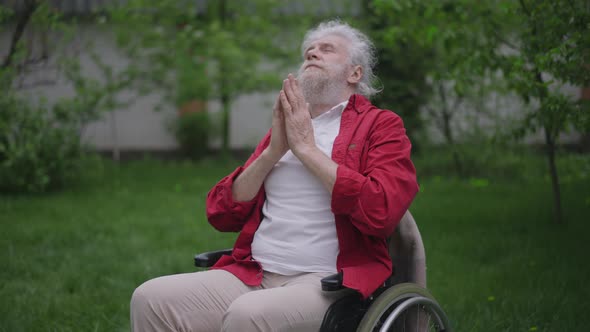 Senior Disabled Man in Wheelchair Praying Outdoors in Green Spring Garden