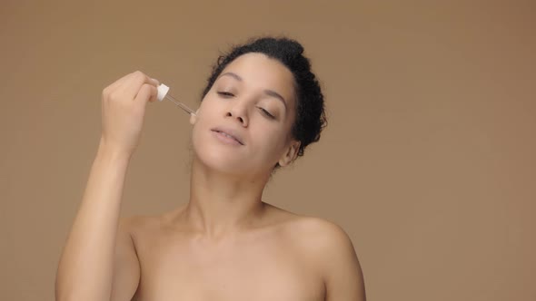 Beauty Portrait Young African American Woman Applying Skincare Serum on Face Rubbing Gently with