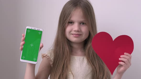 Pretty Little Girl Shows Phone with Green Screen Mock Up Cellphone Mobile Telephone and Red Heart