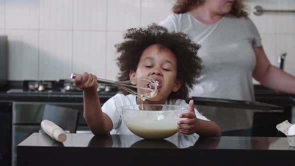 Mixed Family Baking Black Little Girl Eating Raw Liquid Dough From the Whisk and Her Mother Brings