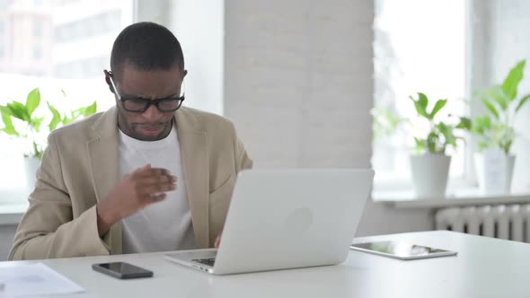 African Man Coughing While Using Laptop in Office