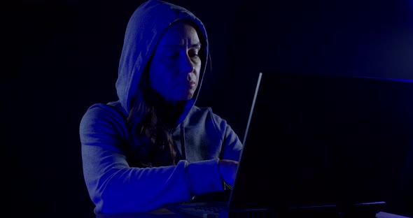 Female Hacker Sitting in the Dark with His Laptop and Tries To Crack the Code Software. Colored Neon