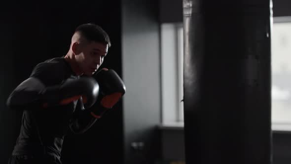 Athletic Man Boxer Wearing Sports Clothes Hitting the Punching Bag in the Gym