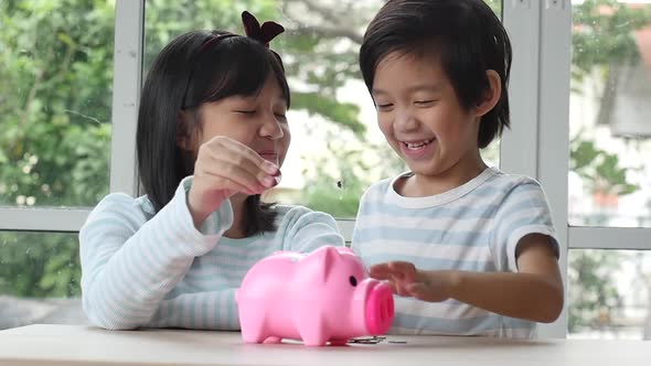 Cute Asian Child Putting A Coin Into A Piggy Bank