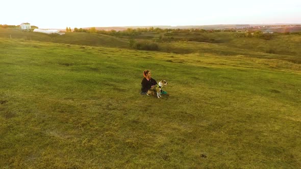 Girl petting American Staffordshire terrier on hill at sunset