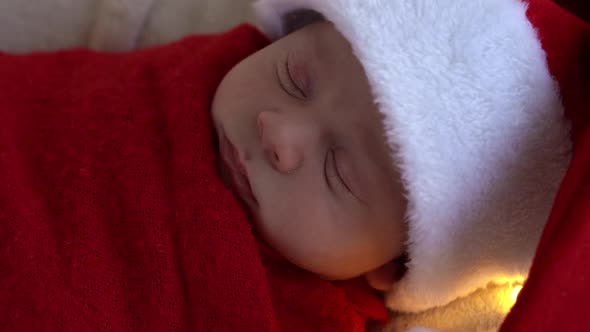 Close Up Portrait First Days Of Life Newborn Cute Funny Sleeping Baby In Santa Hat Wrapped In Red