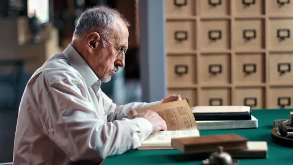 Elderly Man Reading Book Studying Materials Preparing to University Lecture at Library Workplace