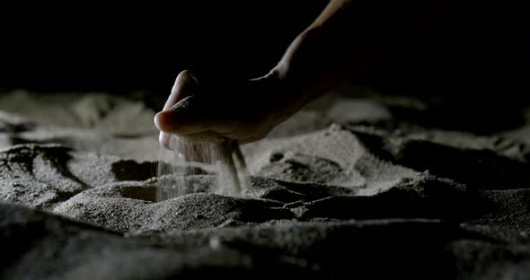 Person Takes Handful of Dry Sand and Holds in Darkness