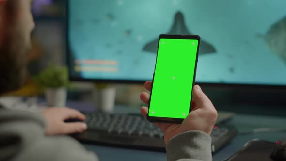 Competitive Gamer Looking at Smartphone with Green Screen Display