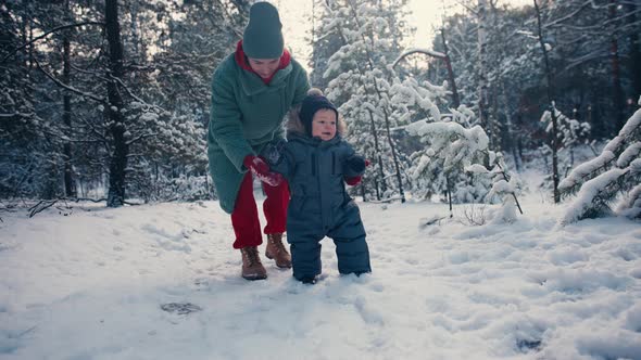 Mother Learning Her Little Baby Son His First Steps in the Snow Forest