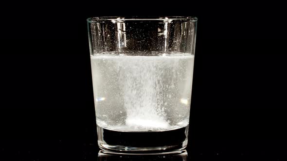 Pill Aspirin Falling Down in Glass with Water on Black Background