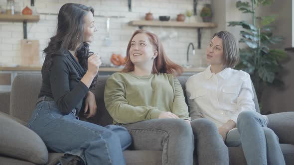 Three Cheerful Beautiful Women Sitting on Couch Talking Indoors