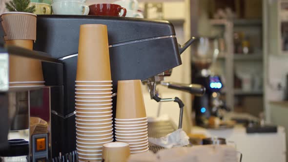 Cardboard Disposable Takeaway Coffee Cups are Stacked Near a Professional Coffee Machine in a Cafe