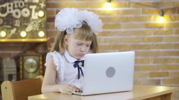 Little Girl Sits at Table and and Typing on the Laptop Keyboard on the Background of a School Class