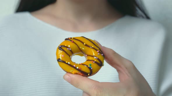 A Woman Dressed in White Clothes Holds Out an Appetizing Donut