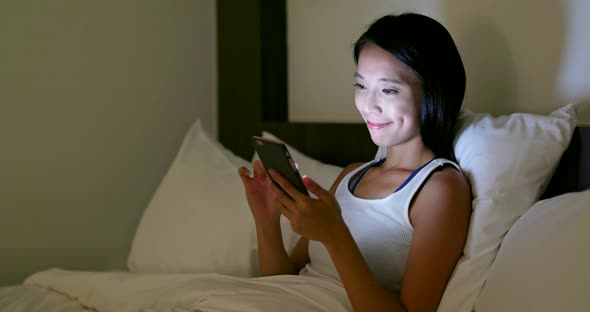 Woman use of mobile phone and lying on bed at night 