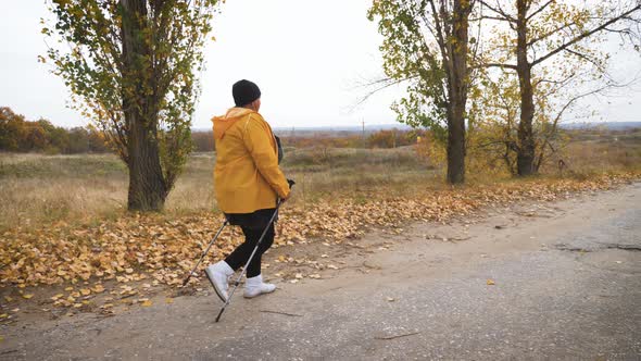 Senior Woman Making Nordic Walking in the Autumn Forest. Nordic Walking Race on Autumn Trail