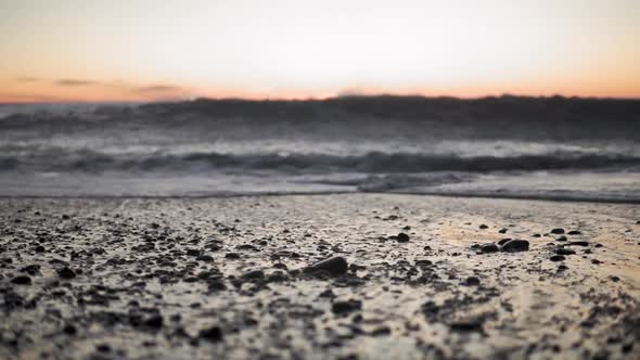 Close up beach waves crashing on shore with sand and pebbles in slowmo