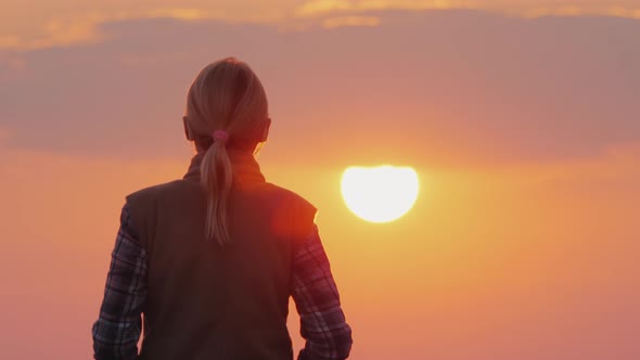 A Silhouette of a Woman Walking Forward Towards the Big Red Sun. Back View