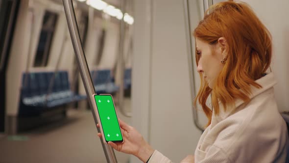 Side view female watching at green screen phone in subway train.